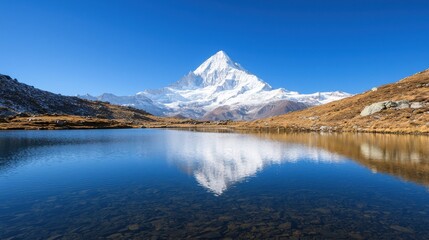 Fototapeta premium A stunning mountain landscape reflected in a serene lake, featuring clear blue skies and a snow-capped peak, surrounded by rocky terrain.