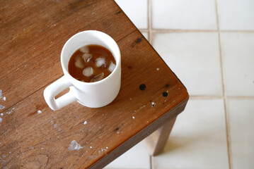 Iced coffee in white cup placed on wooden chair with blurred floor. Iced coffee top view with some space for text. Cafe, cozy, relax, drink, minimal cup, wooden concepts. Cold fresh coffee at home.