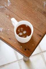 Iced latte coffee in white cup placed on wooden chair in vertical image. Top view iced coffee cup with concept of cafe at home, relaxation, cold, cozy, minimal, and fresh drink. Ice cube in coffee.