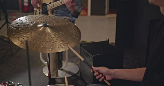 A jazz trio practices in their rehearsal space. The drummer plays the ride cymbal while the bass player plays his bass guitar.
