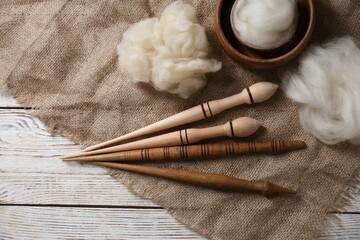 Soft wool and spindles on white wooden table, flat lay