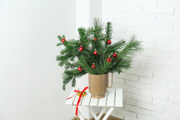 Beautiful Christmas composition of decorated fir and pine tree branches on stool at home