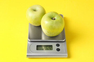 Electronic kitchen scale with apples on yellow background, closeup