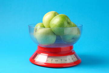 Kitchen scale with apples on light blue background, closeup