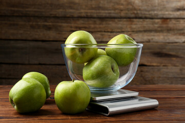 Electronic kitchen scale with bowl of green apples on wooden table, closeup