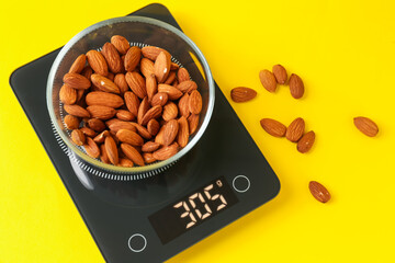 Electronic kitchen scale with bowl of almond nuts on yellow background, flat lay
