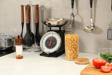 Retro mechanical kitchen scale, other utensils and different food products on white marble...