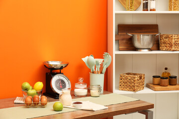 Kitchen scale, products and cooking utensils on wooden table. Space for text