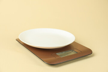 Electronic kitchen scale with plate on beige background, closeup
