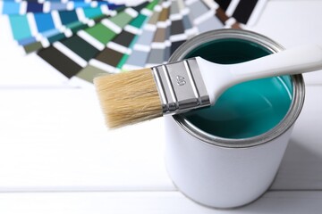 Can of bright paint, brush and color palettes on white wooden table, closeup
