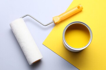 Can of yellow paint and roller on color background, flat lay
