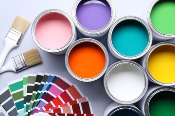 Cans of bright paints, brushes and color palettes on grey background, flat lay