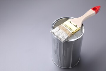 Can of white paint and brush on grey background, closeup. Space for text