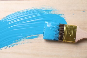 Smear of light blue paint and brush on wooden table, top view