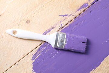 Smear of violet paint and brush on wooden table, top view