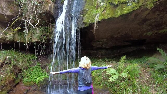 Blonde hiker feeling the water of a waterfall in esles
