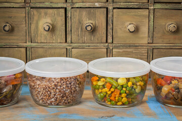 dinner leftovers (buckwheat kasha, vegetables, stir fry)  in glass  containers with drawer cabinet in background