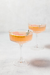 Elegant grapefruit and rosemary cocktails served in crystal glasses with fresh grapefruit slices, set against a light background. Perfect for summer gatherings and holiday party. Refreshing mocktail.