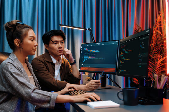 IT developers discussing with point to intelligent website development coder system running data online two screens information technology at neon light room at modern office. Infobahn.