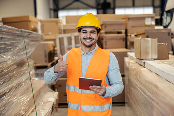 Portrait of transport company manager with tablet giving thumbs up at camera at facility.