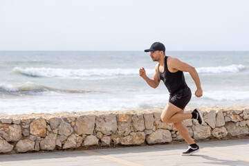 Athletic man running near ocean on sunny day at seaside promenade.