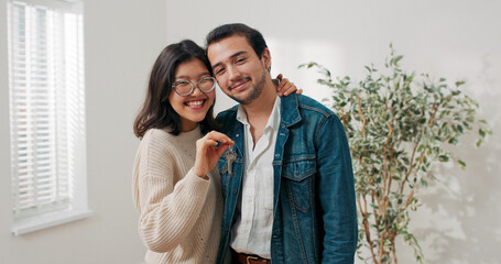 Holding keys in her hand, a happy woman hugs her boyfriend. They stand in their first apartment,...