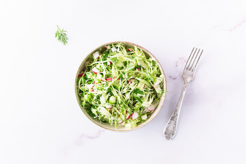 Diet low carb spring salad with juice cabbage, cucumbers, dill, parsley, green onion, small radish and olive oil on light marble table top view. Healthy vegan food concept.