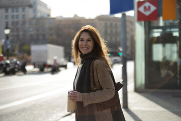 Smiling businesswoman holding reusable coffee cup near subway entrance