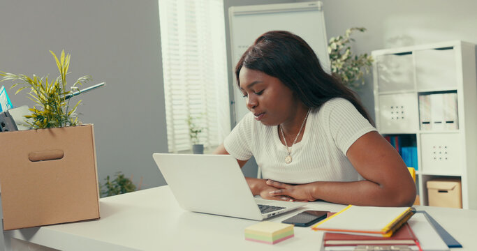 Long-time employee of company's marketing department sits in new office, got a promotion, talks via laptop to a colleague, video call, gossips via social network, webcam, girl waves goodbye