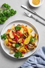 Baked vegetables potatoes, cabbage, pepper and onion in a plate on a light background with fresh parsley.