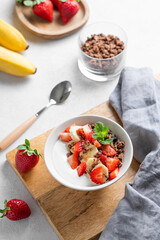 Natural Greek yogurt with homemade chocolate granola, strawberries and banana in a bowl