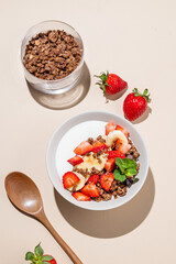 Greek yogurt with chocolate granola, strawberries and banana in a bowl on a beige background