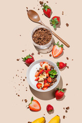 Flat lay of Greek yogurt with chocolate granola, strawberries and banana in a bowl on a beige background