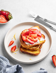 Toasted bread with cream cheese and strawberries on a plate on a light background with fresh berries.