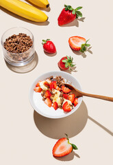 Greek yogurt with chocolate granola, strawberries and banana in a bowl on a beige background
