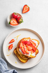Toasted bread with cream cheese and strawberries on a plate on a light background with fresh berries.