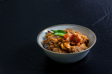 Beef masala or roast, Kerala-style homemade recipe, garnished with curry leaves and served in a white bowl against a black background.