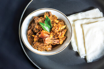 Rice Pathiri with beef masala or roast, a Kerala-style homemade recipe, garnished with curry leaves and served in a white bowl against a black background.