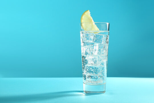 Soda water with lemon and ice cubes in glass on light blue background