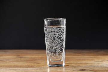 Refreshing soda water in glass on wooden table against black background, closeup