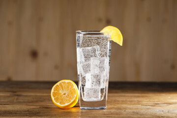 Refreshing soda water with ice cubes in glass and cut lemon on wooden table, closeup