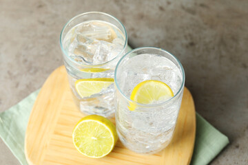 Refreshing soda water with ice cubes and cut lemon in glasses on grey textured table, closeup