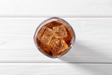 Sweet soda water with ice cubes in glass on white wooden table, top view