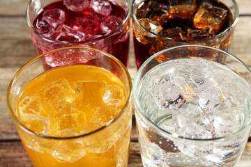 Soda water of different flavors with ice cubes in glasses on table, closeup