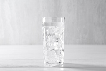 Refreshing soda water with ice cubes in glass on white wooden table