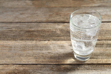 Soda water with ice cubes in glass on wooden table, closeup. Space for text