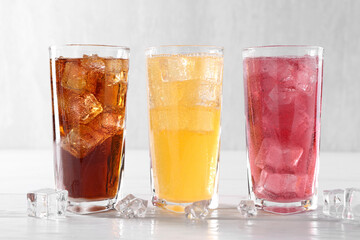 Soda water of different flavors in glasses with ice cubes on white wooden table