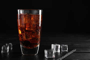 Sweet soda water in glass with ice cubes on black wooden table, space for text