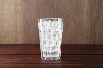 Refreshing soda water with ice cubes in glass on wooden table