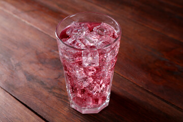 Sweet soda water with ice cubes in glass on wooden table, closeup
